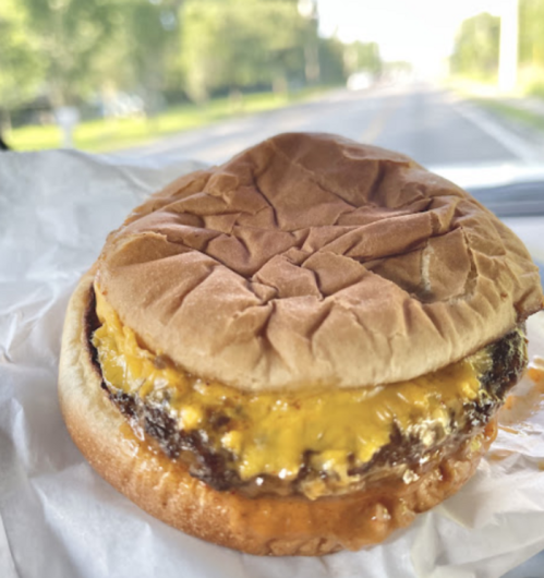 A close-up of a cheeseburger with melted cheese on a toasted bun, sitting on a white wrapper in a car.