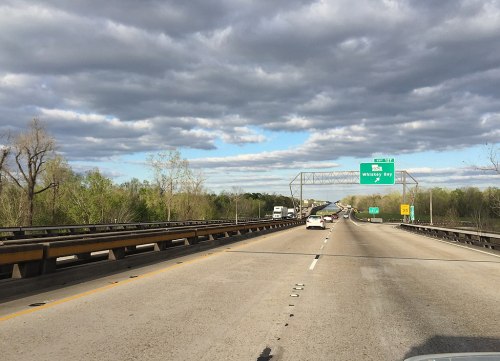 A highway scene with vehicles, green trees, and a cloudy sky, featuring a sign for Whiskey Bay.