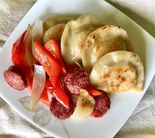 A plate of pierogi with sautéed red peppers, onions, and sliced sausage.