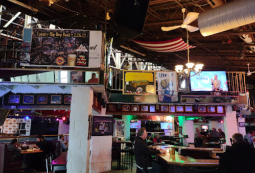 Interior of a lively bar with various decorations, including posters, TVs, and an American flag hanging above.