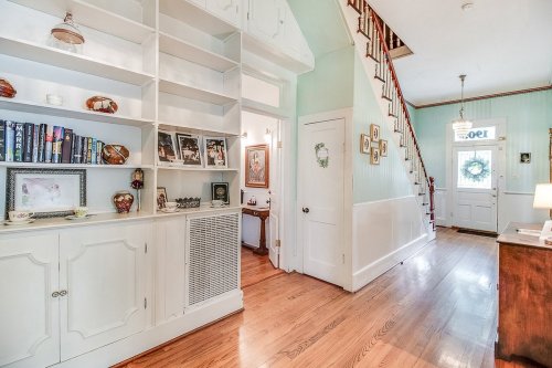 Bright hallway with wooden floors, built-in shelves, and a staircase leading to the upper level. Decorated with personal items.