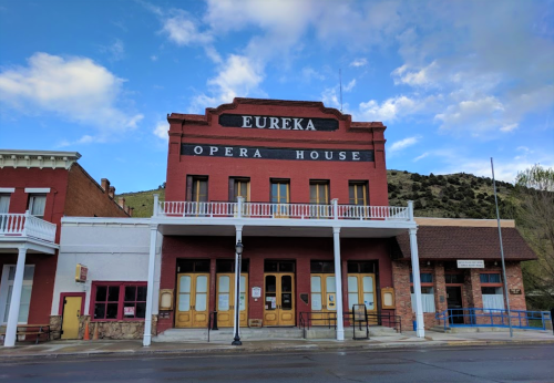 Historic Eureka Opera House with red brick facade, white balcony, and mountains in the background under a blue sky.
