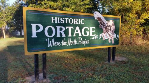 Sign reading "Historic Portage: Where the North Begins," surrounded by trees and grass.