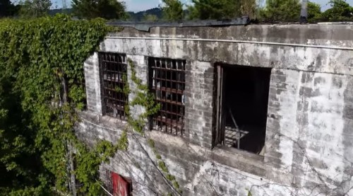 Abandoned building with ivy-covered walls and barred windows, showing signs of decay and neglect.