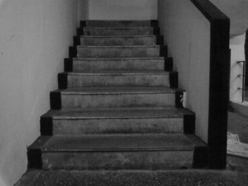 A monochrome image of a set of concrete stairs leading upward, with black edges on each step.