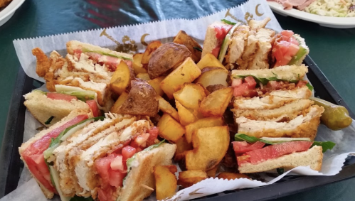 A platter of sandwiches with fried chicken, lettuce, and tomato, accompanied by golden-brown potato wedges.