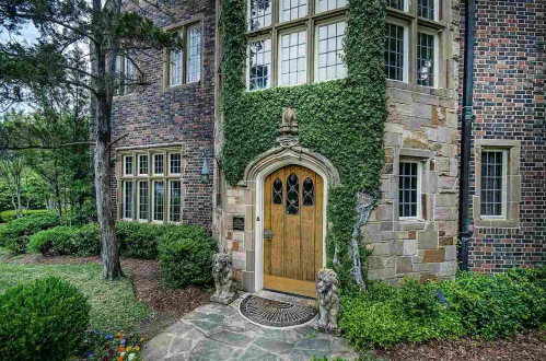 A charming brick house entrance with ivy, featuring a wooden door and stone lion statues flanking the doorway.