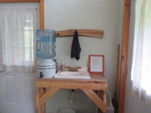 A simple sink setup with a water cooler, wooden shelf, and framed document in a light-colored room.