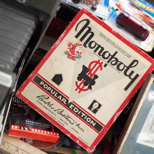 A vintage Monopoly board game box among various items on a cluttered shelf.