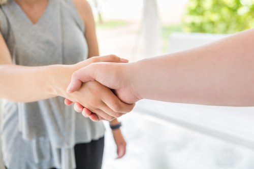 Two people shaking hands, symbolizing agreement or partnership, with a blurred background of greenery.