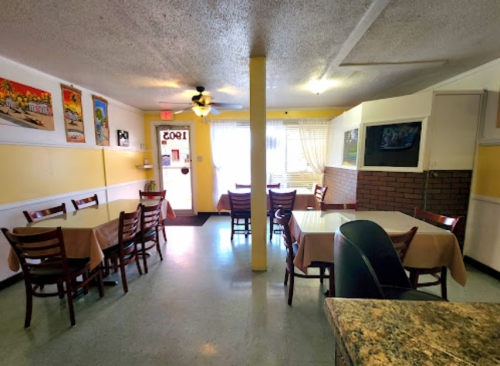 Cozy restaurant interior with tables, yellow walls, and artwork, featuring a door leading outside and a TV on the wall.