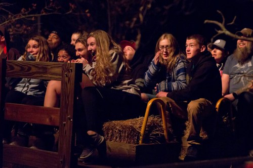 A group of young people sitting on a wooden bench, laughing and enjoying a nighttime event, surrounded by hay bales.