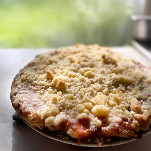 A freshly baked pie with a crumbly topping, sitting on a countertop with a blurred green background.