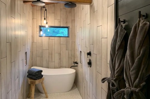 A modern bathroom featuring a freestanding tub, wooden accents, and stylish lighting. Soft towels hang nearby.