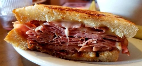 Close-up of a grilled sandwich filled with layers of sliced ham and melted cheese on toasted bread.