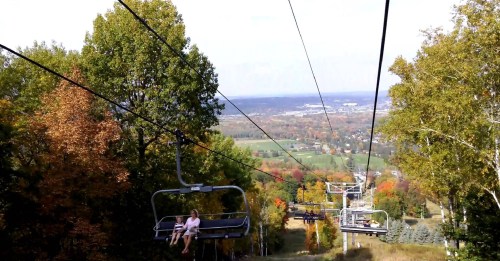 A scenic view from a ski lift, showing colorful autumn trees and a valley below.