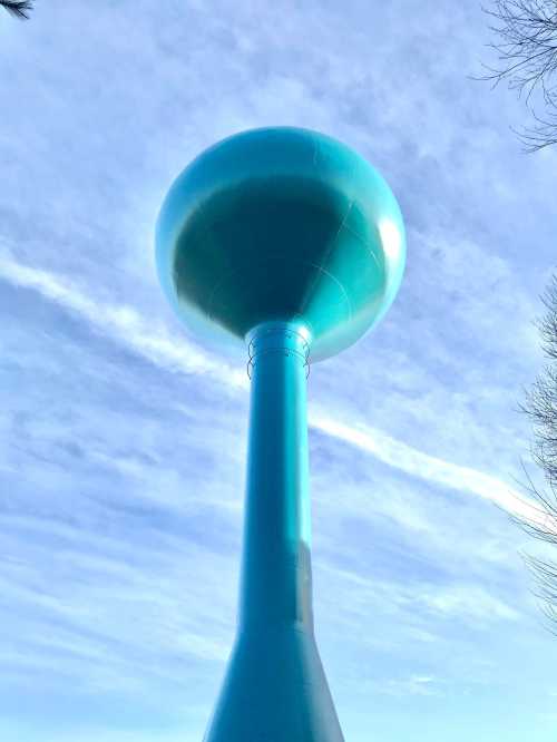 A tall, turquoise water tower against a blue sky with wispy clouds.