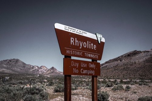 Sign for Rhyolite Historic Townsite, stating "Day Use Only, No Camping," with desert landscape in the background.