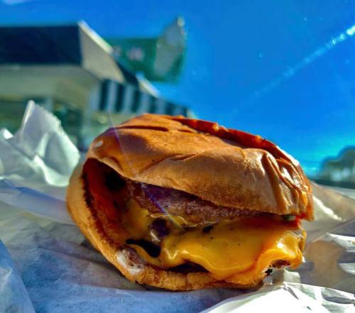 A close-up of a cheeseburger with melted cheese, set against a bright blue sky and a blurred background.