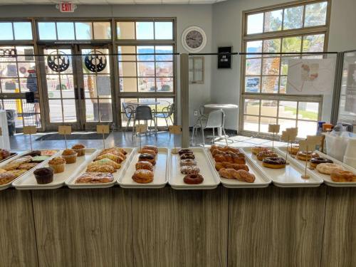 A display of various donuts on trays in a bright, modern shop with large windows and seating.