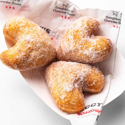 Three heart-shaped, sugar-dusted pastries in a paper basket.