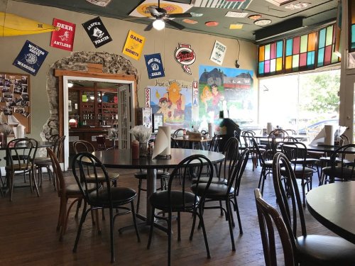 A cozy restaurant interior with wooden tables, chairs, colorful banners, and a mural on the wall.