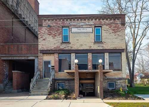 Historic brick building with large windows, a sign reading "The 1912," and a staircase leading to the entrance.