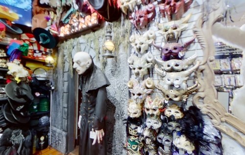 A spooky display featuring a life-sized figure and various decorative masks on a wall in a costume shop.