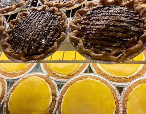 Two types of pies on display: one with chocolate drizzle and nuts, and several lemon cream pies with graham cracker crusts.