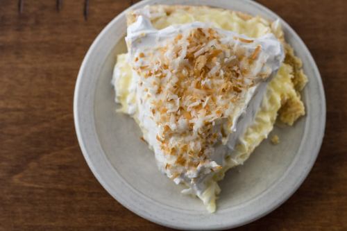 A slice of coconut cream pie topped with whipped cream and toasted coconut on a light-colored plate.