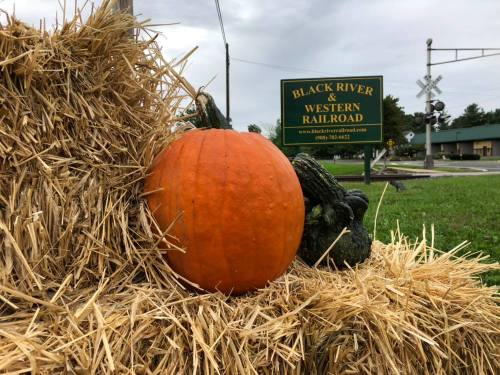 A bright orange pumpkin rests on a haystack near a sign for Black River & Western Railroad.