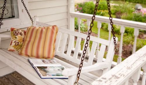 A white swing bench with a colorful pillow and an open book, surrounded by a lush garden.