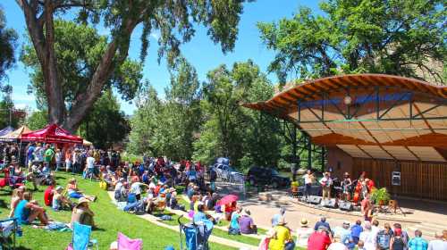 A lively outdoor concert scene with a crowd seated on grass, enjoying a performance on a sunny day.