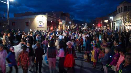 A lively street scene filled with people in colorful costumes during a festive evening event.