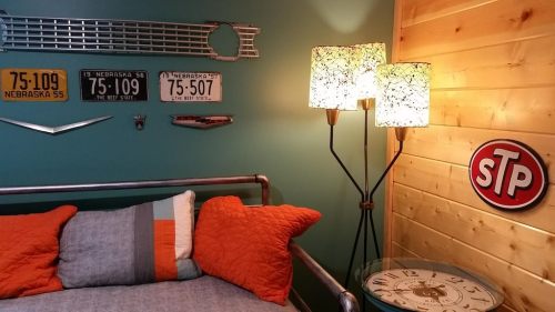 A cozy room featuring a bed with orange pillows, vintage Nebraska license plates, and decorative lamps against a blue wall.