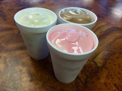 Three cups of soft serve ice cream in vanilla, chocolate, and strawberry flavors on a wooden table.