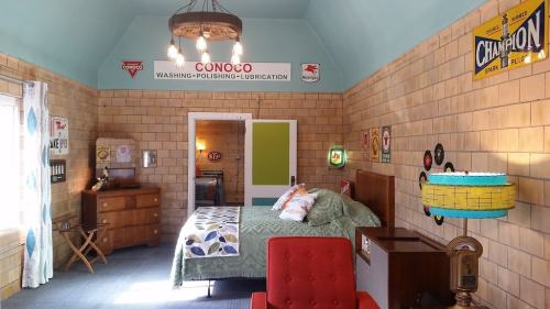 A retro-style bedroom with a green bedspread, vintage signs, and colorful decor, featuring a red chair and wooden furniture.