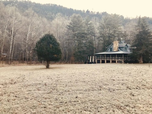 A frosty landscape featuring a large house with a porch, surrounded by trees and mountains in the background.