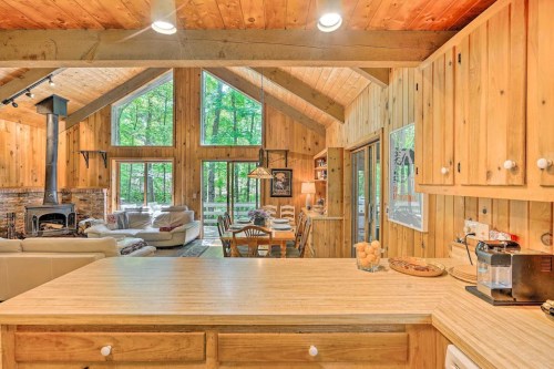 Cozy wooden cabin interior with a spacious living area, large windows, and a dining table surrounded by nature.