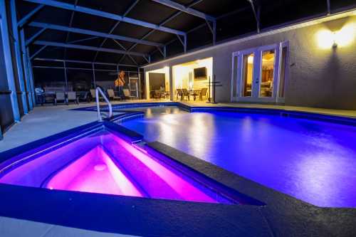 A modern pool area with a blue-lit pool and spa, surrounded by a screened patio and outdoor seating.