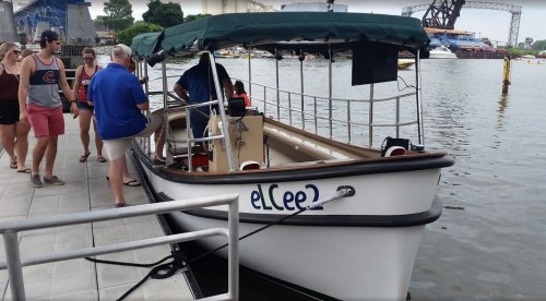 A small boat named "eL Cee 2" docked at a waterfront, with people walking nearby.