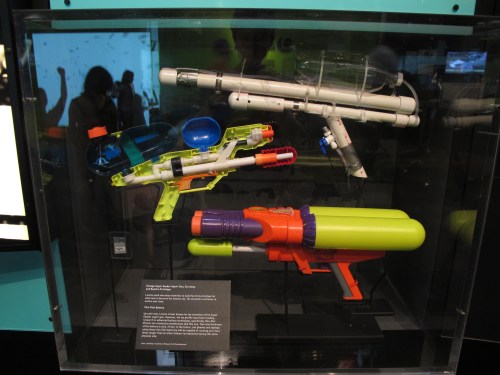 Three colorful toy water guns displayed in a glass case, showcasing various designs and features.