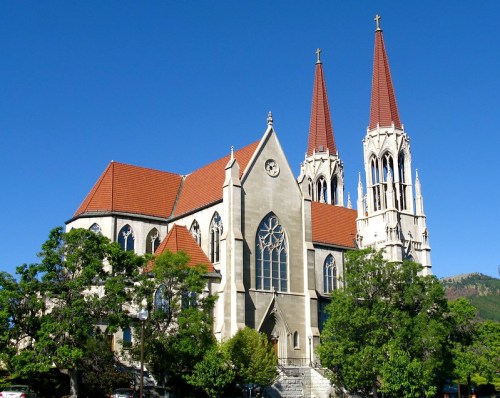 A large church with two tall spires, surrounded by green trees and a clear blue sky.