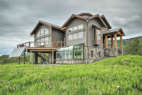 A modern two-story house with large windows, a stone base, and a green lawn under a cloudy sky.