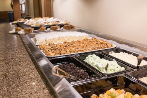 A buffet table featuring various dishes, including stuffing, rice, and desserts in trays.