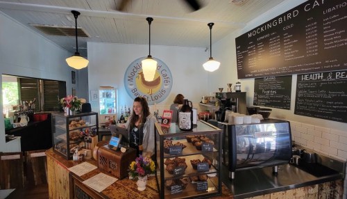 A cozy café interior with a wooden counter, menu boards, and a barista serving customers. Pastries are displayed prominently.