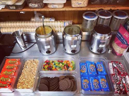 A countertop display with jars of toppings, including candies, cookies, and granola, ready for dessert creations.