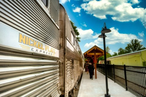 A train labeled "Nickel Plate Express" at a station with a blue sky and clouds in the background.
