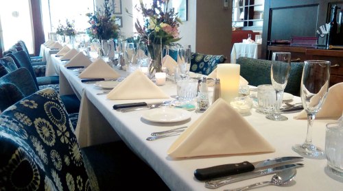 A beautifully set dining table with elegant tableware, folded napkins, and floral centerpieces in a cozy restaurant.