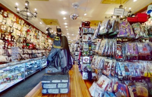 A store aisle filled with costumes and decorations, featuring a Batman statue on a pedestal.
